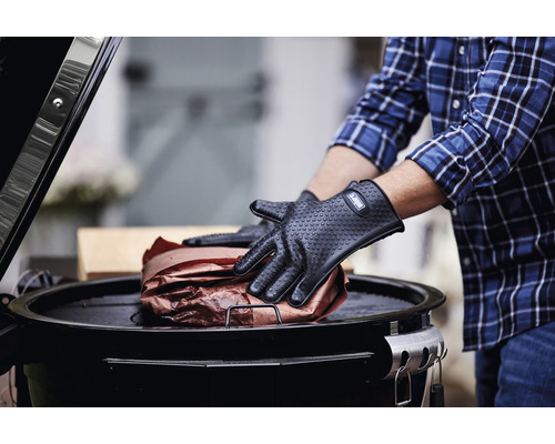 Person med grillhandskar hanterar grillmat på en grill.