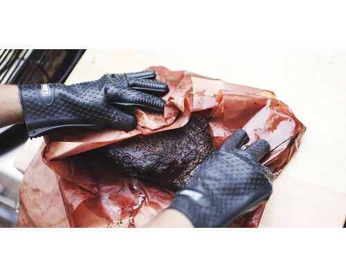 Person med grillhandskar hanterar en bit kött på papper