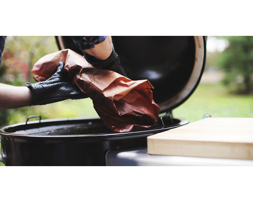 En person med grillhandskar lägger en bit kött i en grill