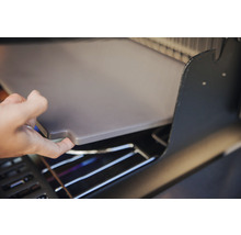 En person lägger en pizzasten i en grill.