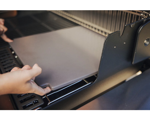 En person placerar en pizzasten i en grill.