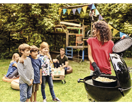 En kvinna grillar i trädgården med barn och en klotgrill.