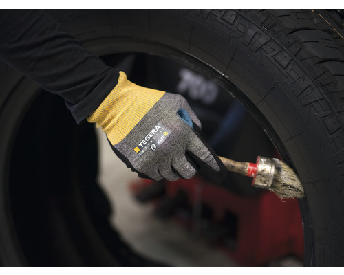 En person bär arbetshandskar och bearbetar ett däck med en pensel.