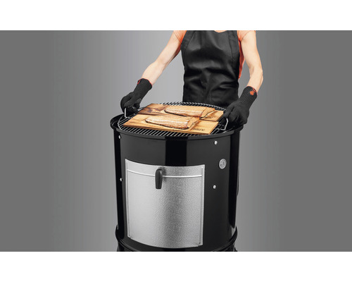 Kvinna med grillhandskar förbereder fisk på en kolgrill