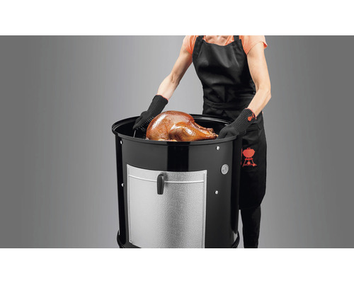 Kvinna lägger kalkon i vattenrökgrill. Weber-logotyp på förklädet.