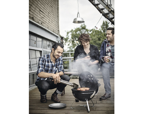 Tre personer grillar korv på ett trägolv med en klotgrill.