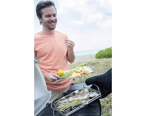 Man grillar fisk och grönsaker på stranden.