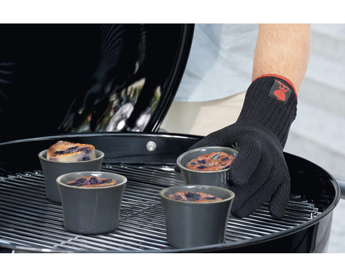 Person med grillhandske som placerar ugnsformar med blåbärskaka på en grill.