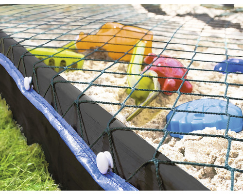 Närbild av en sandlåda med nätskydd och leksaker i sanden