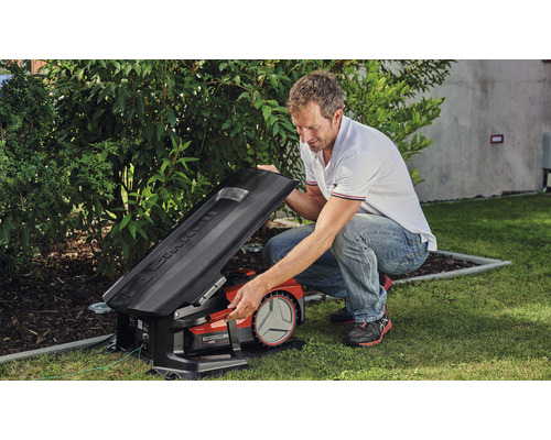 En man öppnar locket på en robotgräsklippare i trädgården.