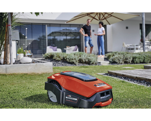 En röd robotgräsklippare står på en gräsmatta framför ett bostadshus.