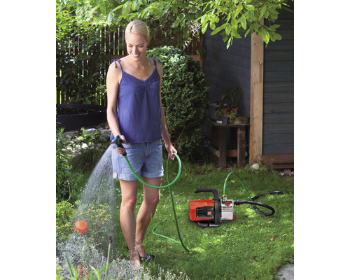 Kvinna vattnar trädgård med trädgårdspump och trädgårdsslang.