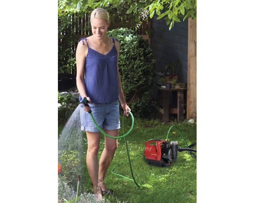 Kvinna vattnar trädgården med trädgårdspump och trädgårdsslang
