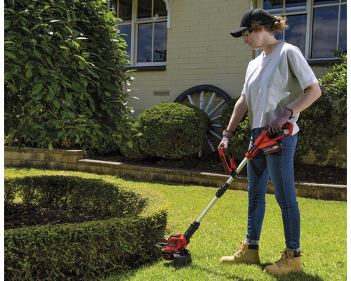 Kvinna använder sladdlös grästrimmer i trädgården.