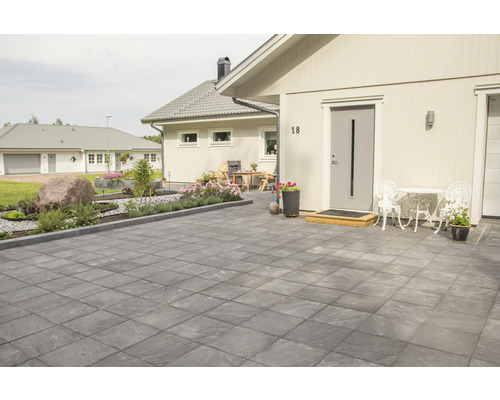 Utsida av ett hus med en stenlagd uppfart, trädgård och sittplatser