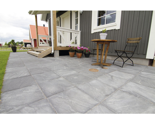 Uteplats med grå plattor, bord och stol framför huset
