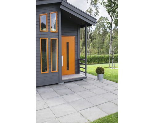 Vy över ett hus med en grå fasad, fönster och en ytterdörr.