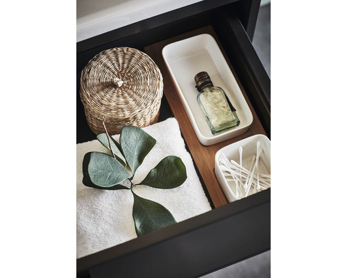 Öppen låda med flätad korg, handduk, behållare och bomullspinnar för badrumsartiklar.
