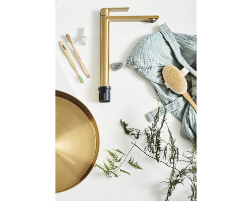 Guldfärgad tvättställsblandare med badrumstillbehör på vit bakgrund
