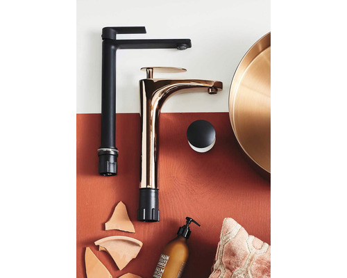 Två tvättställsblandare i svart och koppar på en hylla med badrumstillbehör.