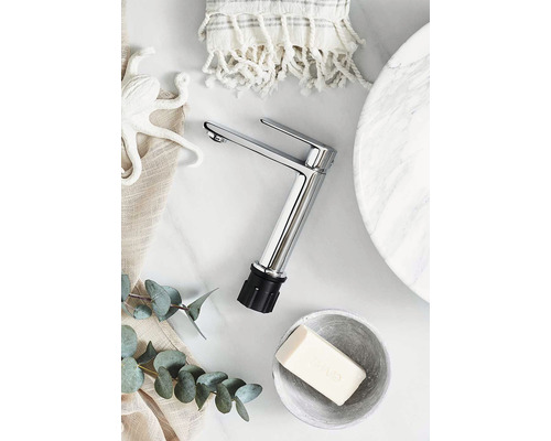 Bild av en kran med handduk, tvål, dekoration och bladverk på en marmoryta.