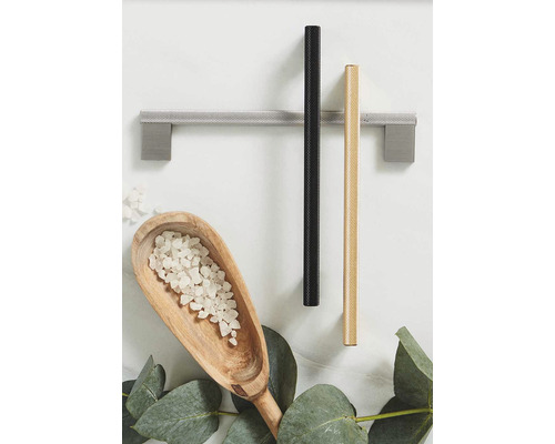 Tre möbelhandtag i silver, svart och guld, tillsammans med en träskopa med badsalt och eukalyptusblad på ett bord