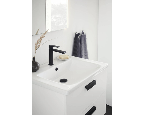 Tvättställ med svart kran, tvål och handdukar i ett ljust badrum.