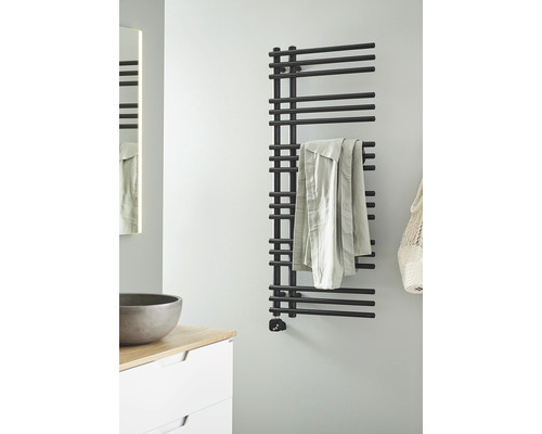 Badrum med svart handdukstork på väggen bredvid handfat och spegel.