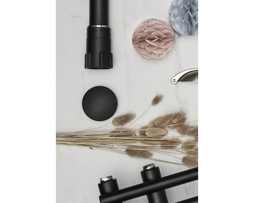 Dekorativ scen med ett svart möbelben, en svart möbelknopp, prydnadsgräs och pappersbollar.