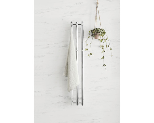 Kromfärgad handdukstork med handduk och krukväxt på en vägg