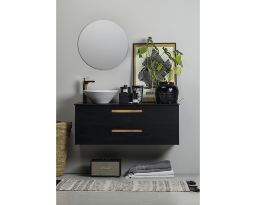 Badrum med rund spegel, handfat, underskåp med lådor och dekorationer.