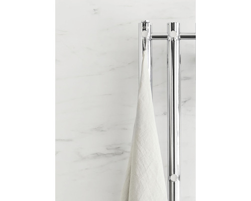Handduk hänger på en kromad handdukstork framför en marmorvägg