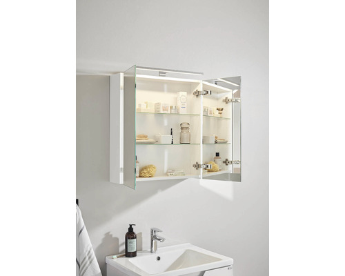 Öppet spegelskåp med belysning ovanför ett handfat i badrummet.