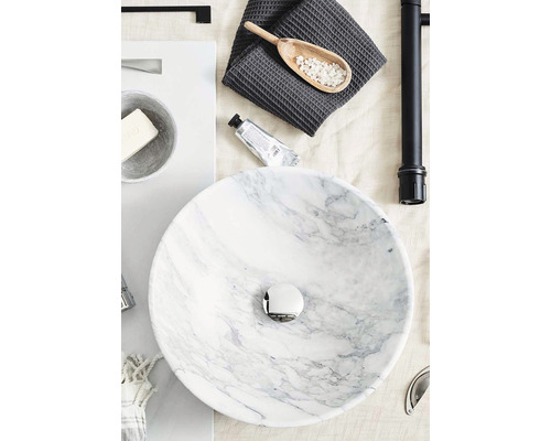 Badrumsstilleben med ett runt marmorhandfat, en handduk, en träsked med badsalt och en handkräm