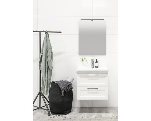 Ljust badrum med tvättställsskåp, spegel, tvättkorg och klädställning.