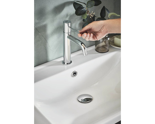 En kromad kran på ett vitt handfat som manövreras av en hand.