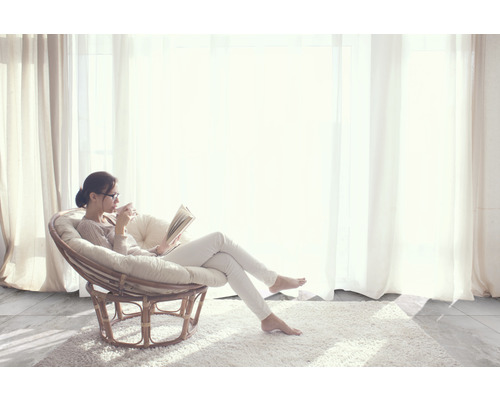 Kvinna läser bok i en rottingfåtölj på en matta framför ett fönster