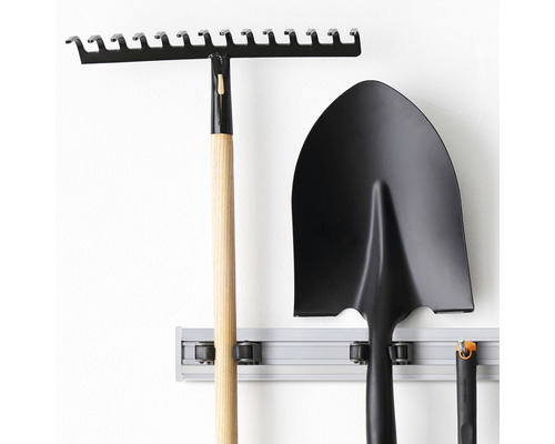 Trädgårdsredskap som räfsa och spade hänger på en väggskena.