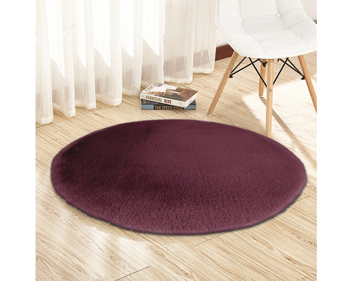 Rund, högflorig matta på trägolv med stol och böcker i bakgrunden.