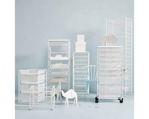 Bild på flera vita trådhyllor i olika storlekar i ett rum, vissa med tygfoder, som erbjuder förvaringslösningar