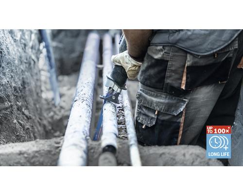 Hantverkare sågar ett rör med en tigersåg i ett dike