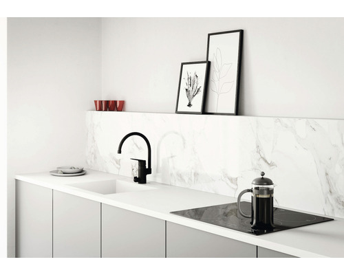 Köksscen med diskho, blandare, spishäll och köksredskap på en bänkskiva framför en marmorvägg