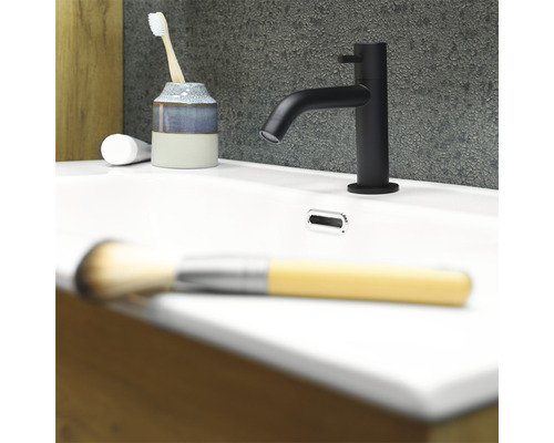 Svart tvättställsblandare på ett vitt handfat med tandborste, tandkräm och sminkborste