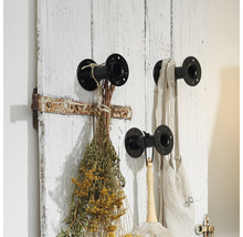 Vägghängare med tre metallkrokar och en dekoration av torkade blommor och tygväska på en vit trävägg