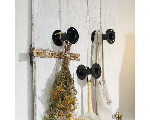 Vägghängare med tre metallkrokar och en dekoration av torkade blommor och tygväska på en vit trävägg