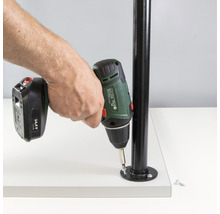 En person fäster en metallkolonn på en vit yta med en sladdlös skruvdragare