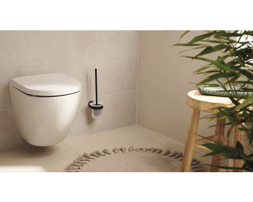 Vägghängd toalett med toalettborste och pall i ett ljust badrum