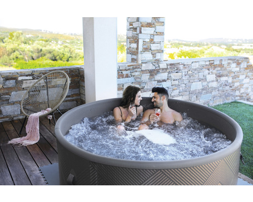 Uppblåsbar bubbelpool med två personer på en terrass med stenelement och en stol