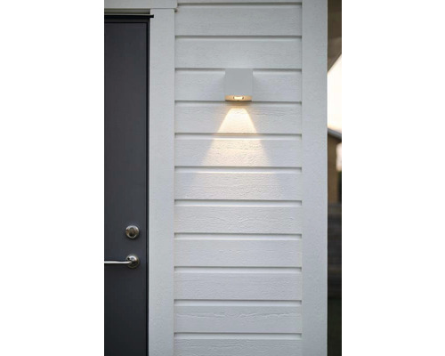 Modern vägglampa i metall bredvid en dörr på en husvägg