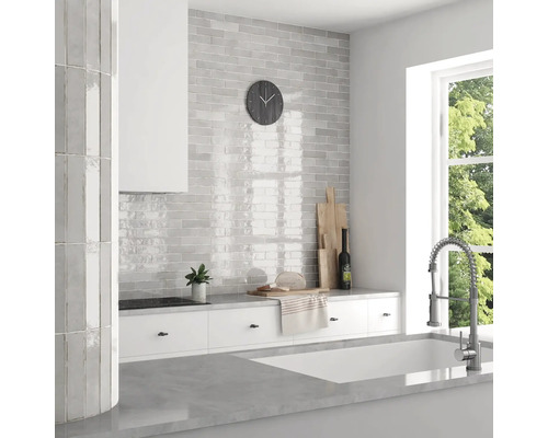 Ljust kök med grå kakel i tegelmönster, vita skåp och ett fönster med utsikt över grönska